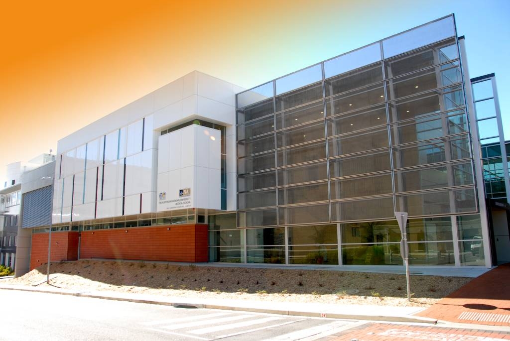 Modern building with a glass facade and partial brick exterior under a gradient orange sky.