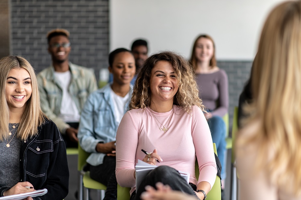 A diverse group of young adults smiling and engaging in a classroom discussion.