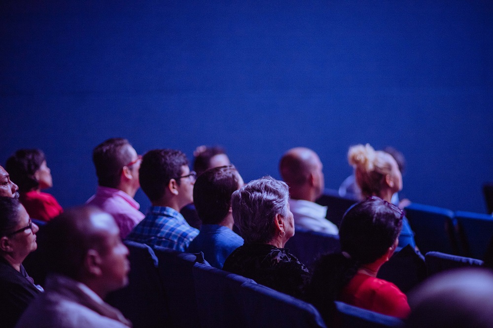 Audience members watching a presentation in a dark room with blue lighting.