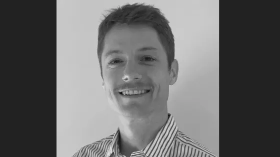 A black and white photo of a smiling man in a striped shirt.