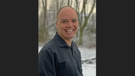 A man smiling at the camera with a snowy forest in the background.