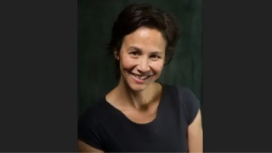 Portrait of a smiling woman with short hair against a dark green background.