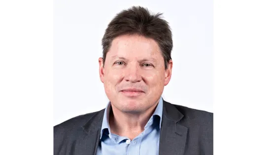 A portrait of a smiling man with brown hair, wearing a blue shirt and dark blazer against a white background.