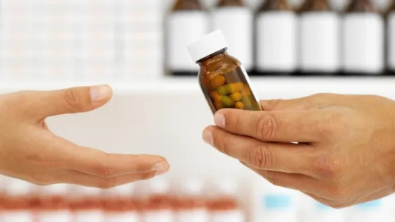 One hand passing a bottle of pills to another hand in a pharmacy setting.