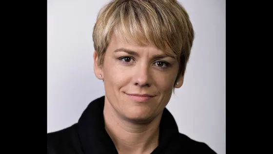 A portrait of a woman with short blonde hair wearing a black top, smiling slightly at the camera.