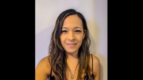 A woman with long, wavy hair smiling at the camera against a light-colored background.