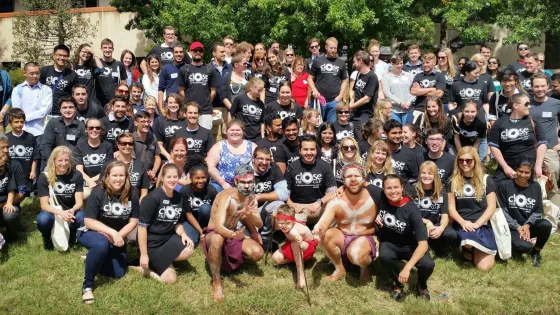 A large group of diverse people wearing matching t-shirts with the text "CLOSE THE GAP" posing together for a group photo outdoors.