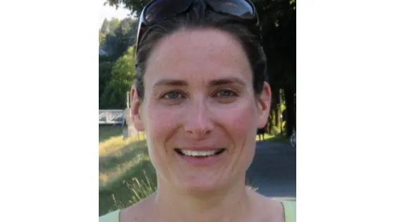 Portrait of a smiling woman with dark hair, sunglasses on her head, wearing a light green top.