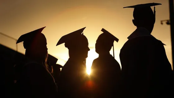 Silhouettes of graduates wearing caps at a sunset ceremony.