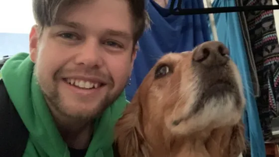 A man in a green hoodie smiling next to a golden retriever looking upwards.