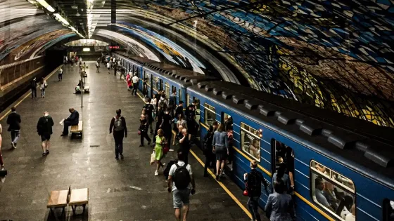 Passengers boarding and exiting a train in a subway station with a vibrant, colorful ceiling mural.