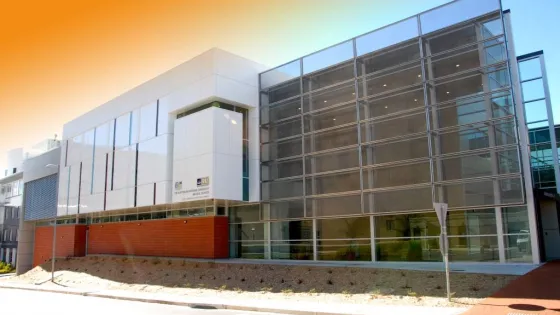 Modern building with a glass facade and partial brick exterior under a gradient orange sky.