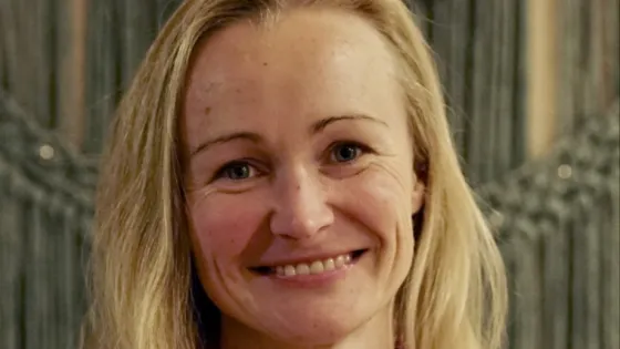 A smiling woman with blonde hair in front of a blurred background.