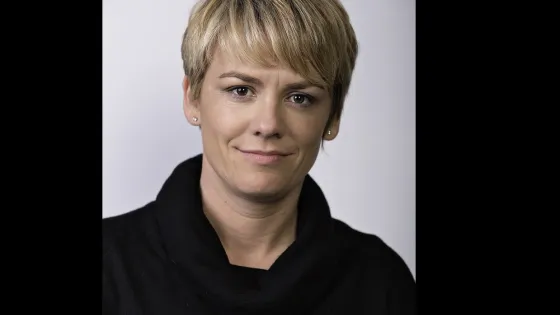 A portrait of a woman with short blonde hair and a black top, giving a subtle smile to the camera.