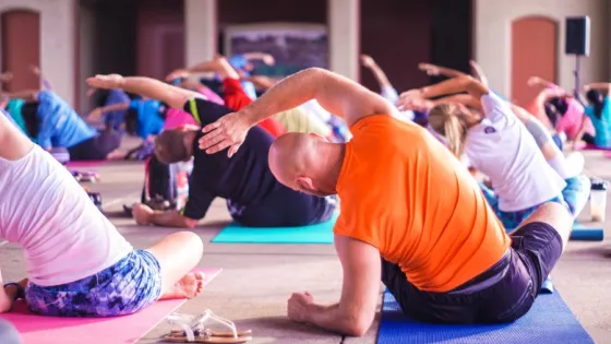 A group of people practicing yoga stretches on mats in an indoor, open space.
