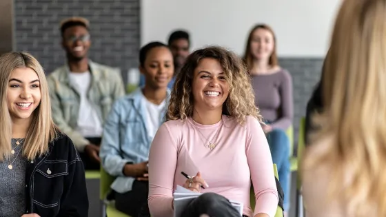 A diverse group of young adults smiling and engaging in a classroom discussion.
