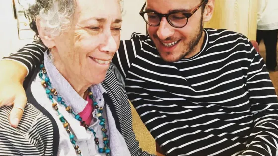 An elderly woman and a young man sitting closely and smiling, sharing a joyful moment together.
