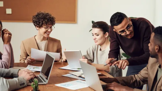 A group of five diverse colleagues actively engages in discussion and review charts around a table in an office setting.