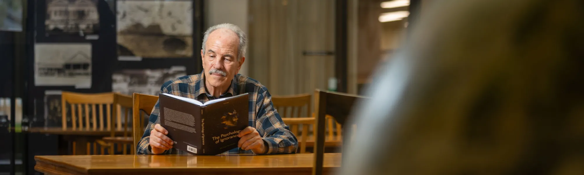 Professor Michael Smithson is inside a library reading a book titled The Psychology of Ignorance