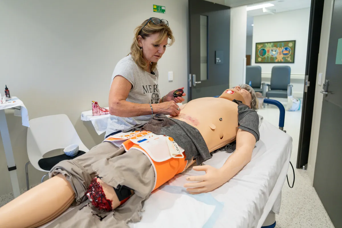 A woman applies fake blood to a dummy