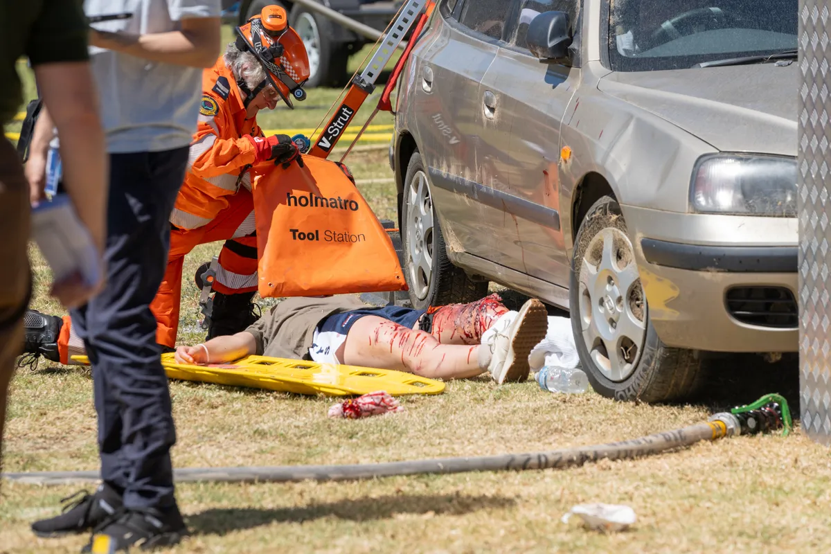 Scene of simulated car accident with patient on the ground being helped by emergency services
