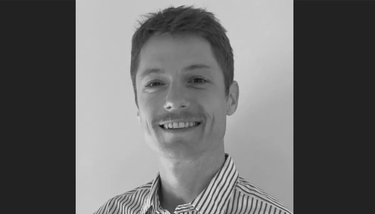 A black and white photo of a smiling man in a striped shirt.