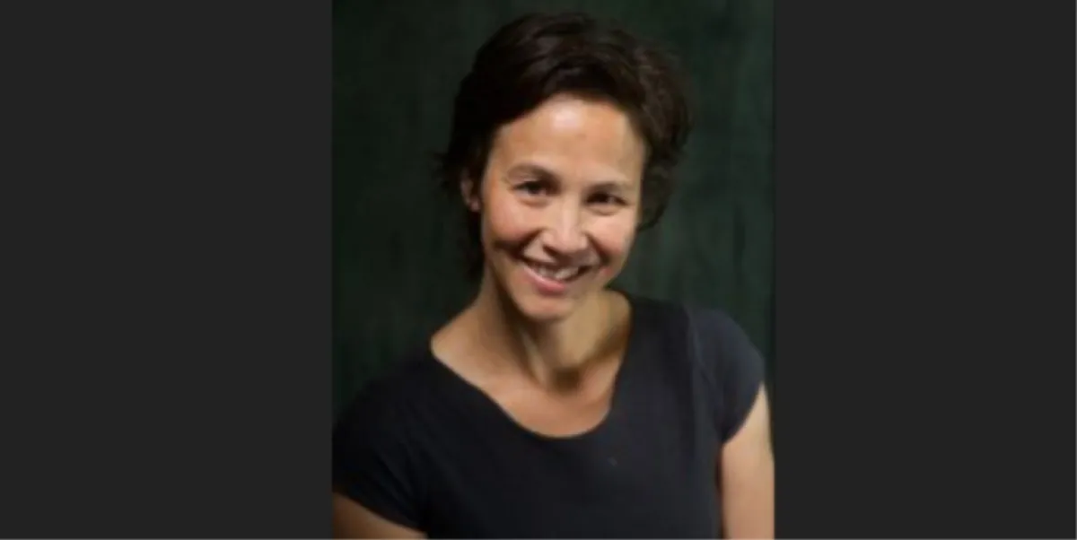 Portrait of a smiling woman with short hair against a dark green background.