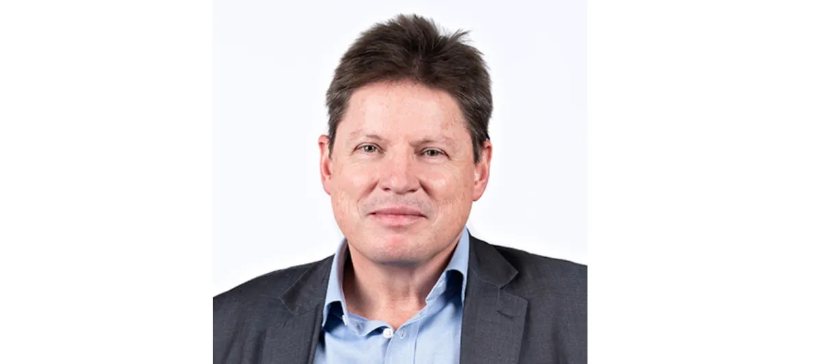 A portrait of a smiling man with brown hair, wearing a blue shirt and dark blazer against a white background.