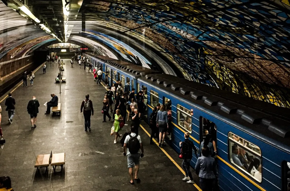 Passengers boarding and exiting a train in a subway station with a vibrant, colorful ceiling mural.