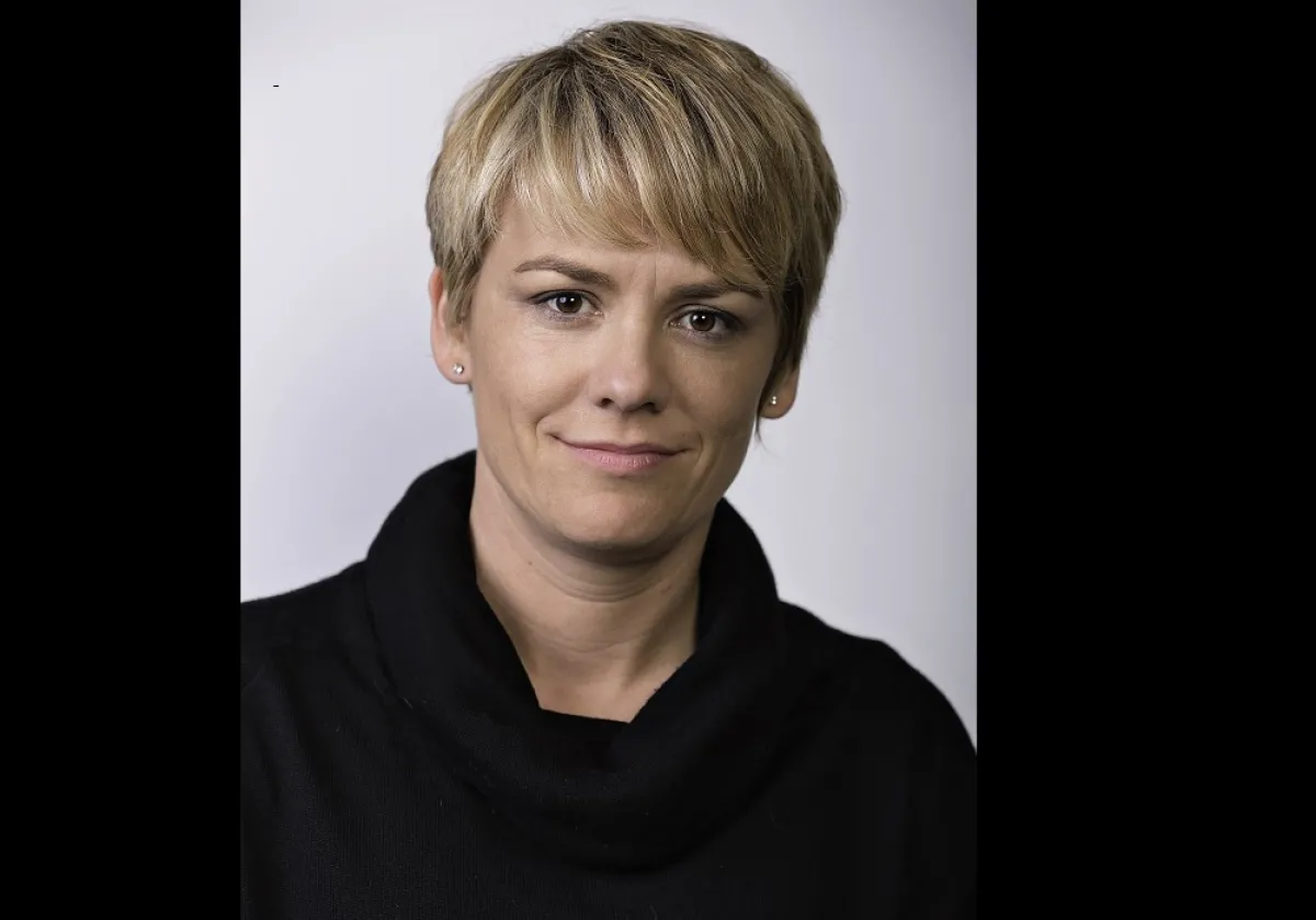 A portrait of a woman with short blonde hair and a black top, giving a subtle smile to the camera.