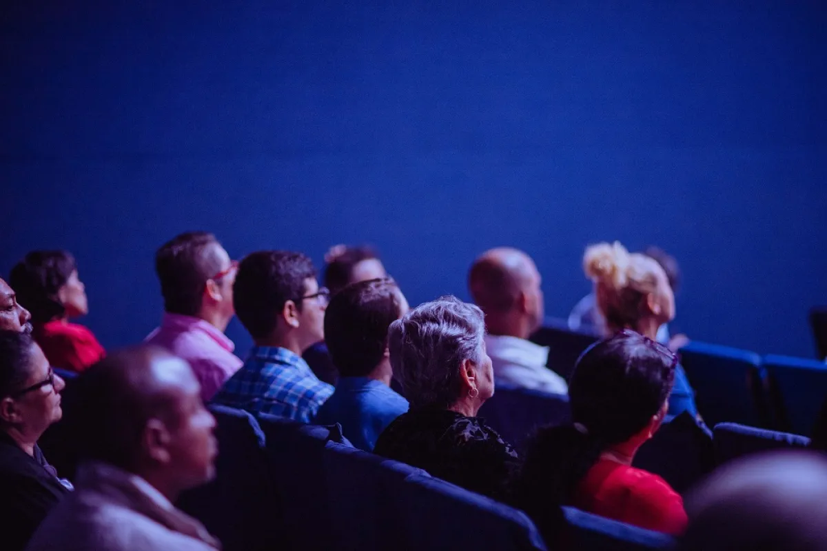 Audience members watching attentively in a darkened theater.