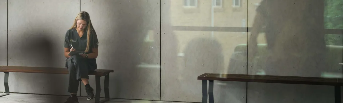 Student sits in hospital foyer writing notes
