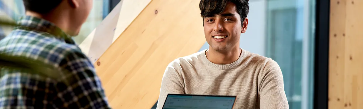 a young man sits at a table with a laptop