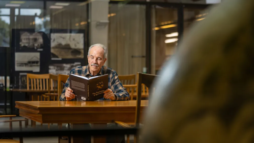 Professor Michael Smithson is inside a library reading a book titled The Psychology of Ignorance