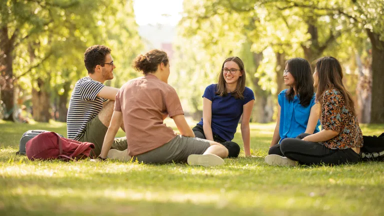 Students sit on the grass under trees at ANU campus