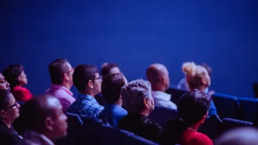 Crowd seated in theatre style seating looking towards presenter
